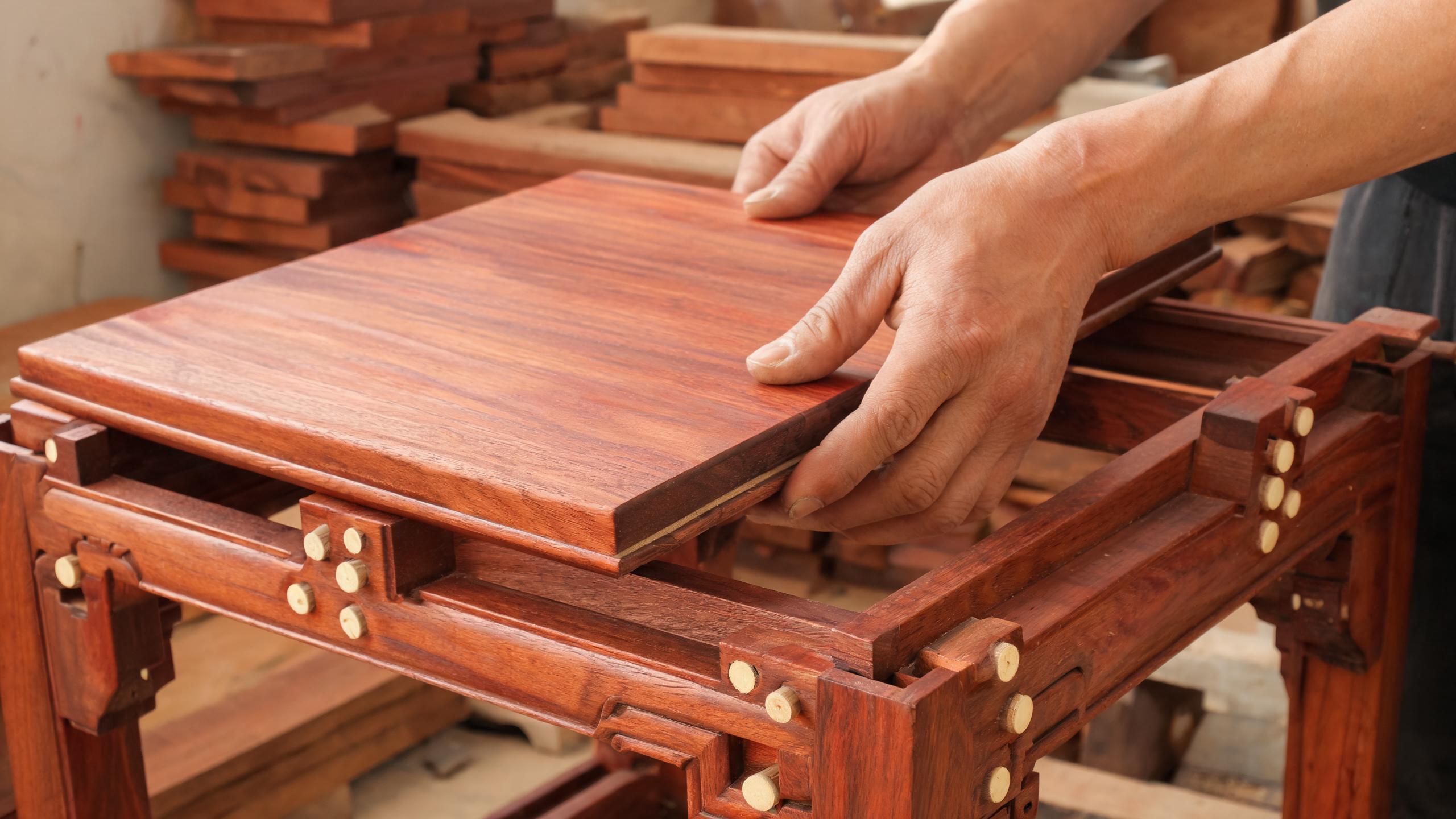 Craftsman fitting a solid rosewood tea table top into a mortise-and-tenon frame with bamboo dowel pins