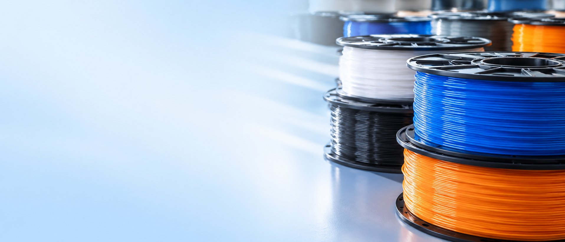 Spools of 3D printing filament in blue, orange, black and white